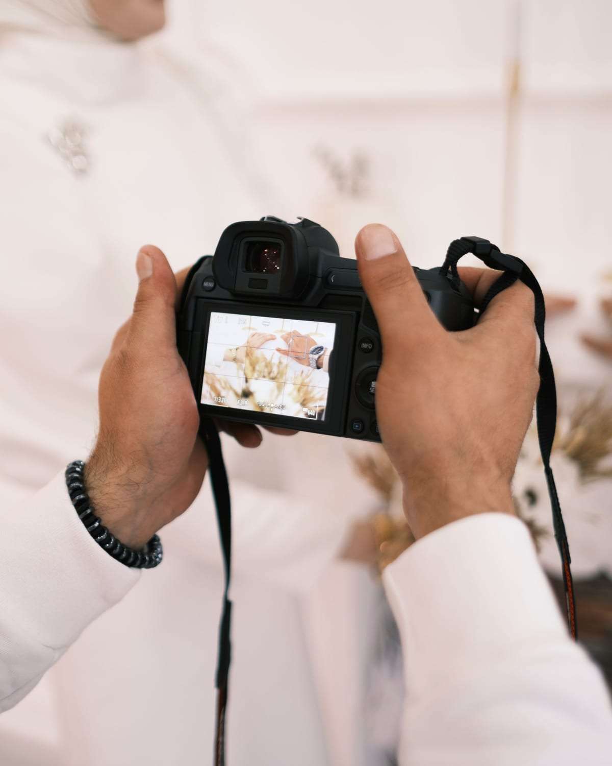 رجل بالثوب والشماغ يحمل كاميرا احترافية ويراجع الصورة على شاشتها